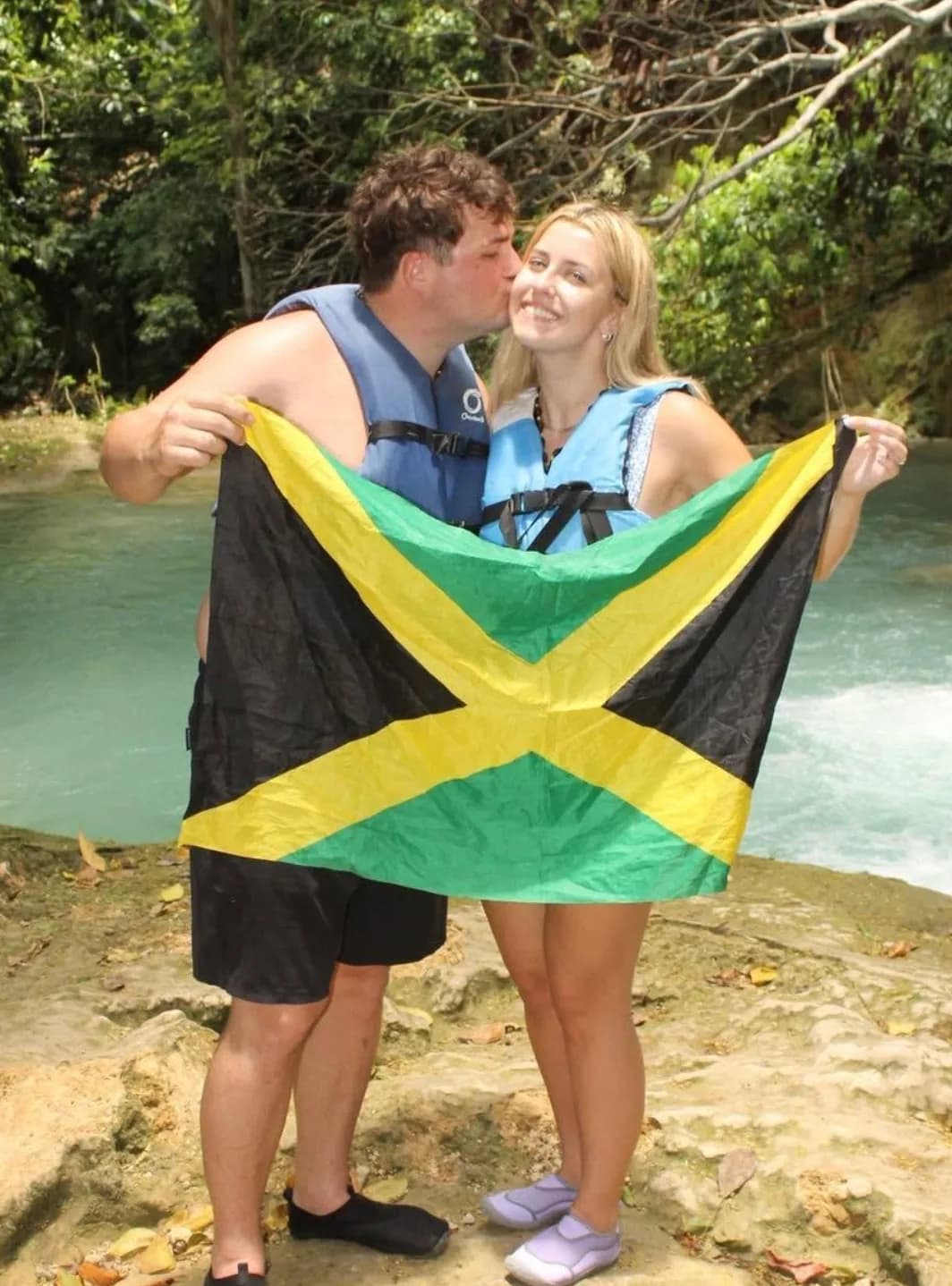 Guests holding a Jamaican flag beside a river waterfall
