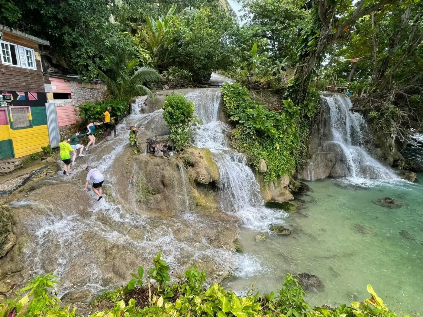 Guests climbing Dunn's River Falls past the colorful riverside houses